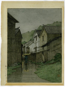 Hasui: Watercolor of an umbrella-carrying pedestrian entering a quiet village in the rain at dusk. There is no known print that corresponds to this image.